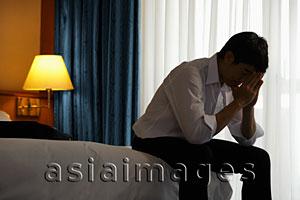 Asia Images Group - Young man sitting on bed with head in hands in the evening