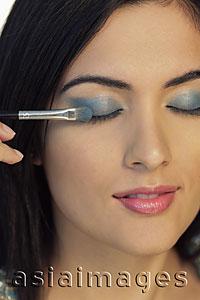 Asia Images Group - Head shot of young woman putting on blue eyeshadow