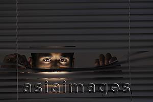 Asia Images Group - Young man looking through blinds with just his eyes visible