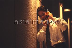 Asia Images Group - Male executive talking on cellular phone under street lamp at night