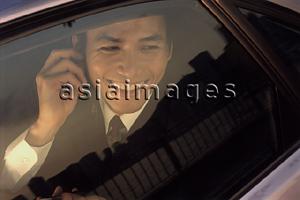 Asia Images Group - Male executive using cellular phone in car, smiling