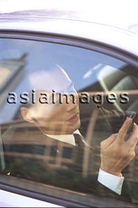 Asia Images Group - Male executive holding cellular phone hands-free set in car