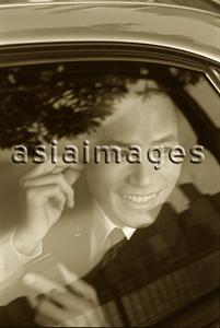 Asia Images Group - Male executive using cellular phone hands-free set in car, smiling