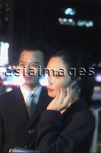 Asia Images Group - Two executives at night, woman using cellular phone