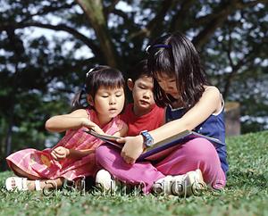 Asia Images Group - Three children sitting on grass reading a book