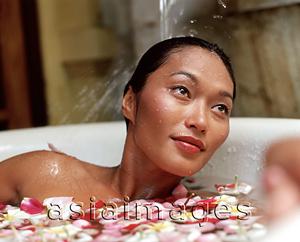 Asia Images Group - Woman in bathtub with flower petals, water pouring on hair