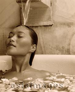 Asia Images Group - Woman relaxing in bathtub with flower petals, water pouring on head