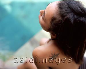 Asia Images Group - Woman sitting by side of swimming pool, tattoo on shoulder