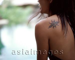 Asia Images Group - Woman sitting by side of swimming pool, tattoo on shoulder