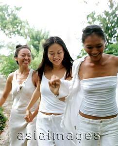 Asia Images Group - Three women wearing white strolling, holding hands, nature in background