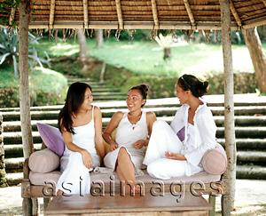 Asia Images Group - Three women wearing white, sitting together on bench talking