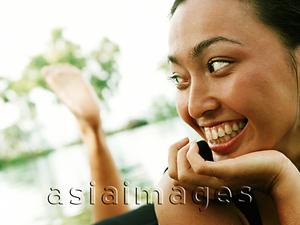 Asia Images Group - Woman with chin on hand looking off camera, water in background.