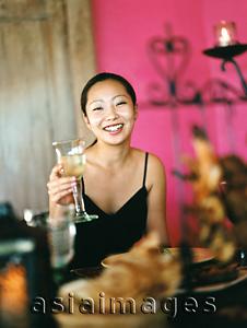Asia Images Group - Woman holding wine glass in dining room, pink background, portrait.