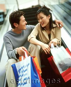 Asia Images Group - Man and woman carrying shopping bags sitting on escalator.