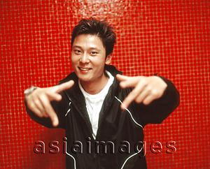 Asia Images Group - Young man smiling and gesturing, orange/red background.
