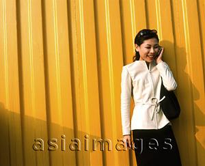Asia Images Group - Woman on cellular phone, yellow background.
