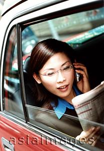 Asia Images Group - Executive woman using cellular phone and reading newspaper in taxi.