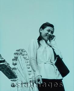 Asia Images Group - Woman on cellular phone, ferris wheel in background.