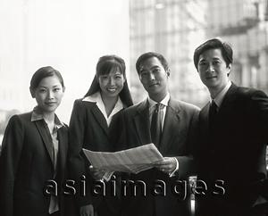Asia Images Group - Male and female executives holding newspaper, buildings in background, portrait.