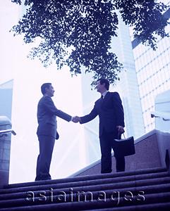 Asia Images Group - Executives shaking hands at top of stairs, buildings in background.