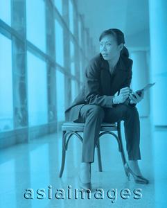 Asia Images Group - Female executive holding PDA sitting by window.