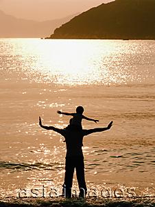 Asia Images Group - Silhouette of man with boy on his shoulders, at the beach at sunset