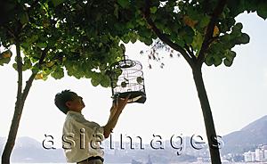Asia Images Group - Man hanging birdcage on tree