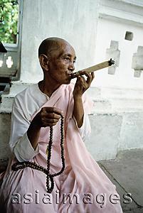 Asia Images Group - Myanmar, Mandalay area, Nun smoking cigar while holding prayer beads