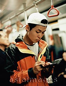 Asia Images Group - Young man on train using PDA.