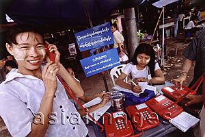 Asia Images Group - Myanmar (Burma), Yangon (Rangoon), A woman wearing homemade makeup makes a telephone call at an open-air public phone station.