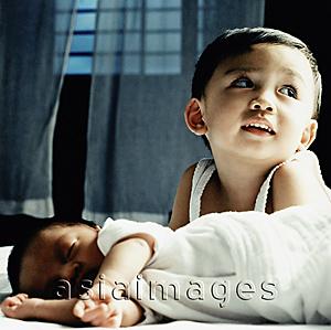 Asia Images Group - Young boy lying on bed behind sleeping baby