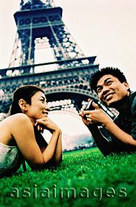 Asia Images Group - Young couple lying on grass, holding camera, Eiffel Tower in background. (high-grained)