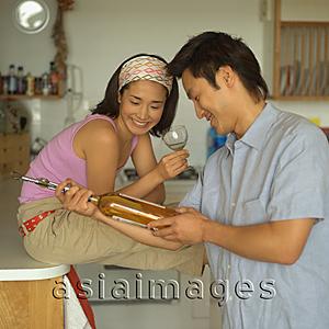 Asia Images Group - Couple in kitchen, looking at wine bottle