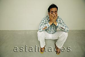 Asia Images Group - Man sitting on floor, hands on face, looking worried, high angle view