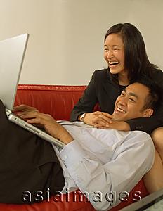 Asia Images Group - Man using laptop, woman hugging him