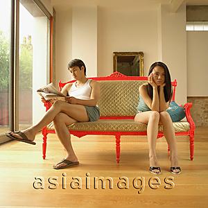 Asia Images Group - Couple sitting apart, man reading, woman with head in hands