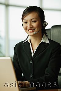 Asia Images Group - Young woman using laptop and wearing hands-free device