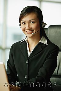 Asia Images Group - Young woman using laptop and wearing hands-free device, looking at camera