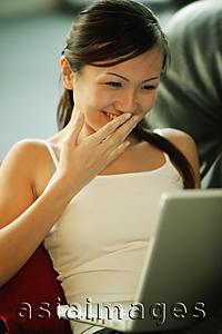 Asia Images Group - Young woman on sofa, using laptop, smiling