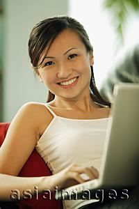 Asia Images Group - Young woman on sofa, using laptop, looking at camera