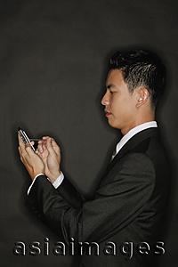 Asia Images Group - Young man using PDA, standing in profile