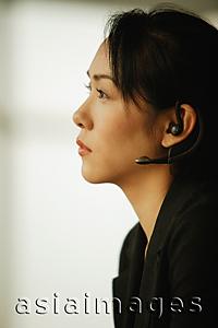 Asia Images Group - Young woman sitting at desk, using hands-free device