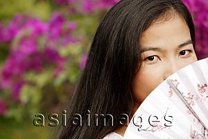 Asia Images Group - Young woman peeking over fan.