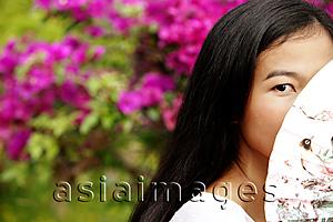 Asia Images Group - Young woman peeking behind a fan.