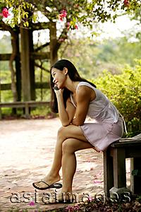 Asia Images Group - Young woman sitting on a bench, using a mobile phone
