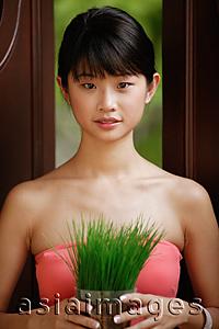 Asia Images Group - Young woman holding plant, looking at camera