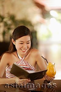 Asia Images Group - Young woman reading menu, drink on the table in front of her