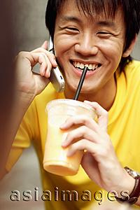 Asia Images Group - Young man on the phone, holding cup and smiling