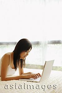 Asia Images Group - Young woman lying on bed, using laptop