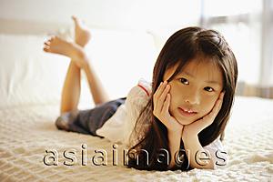 Asia Images Group - Young girl with hands on chin, lying on bed, looking at camera